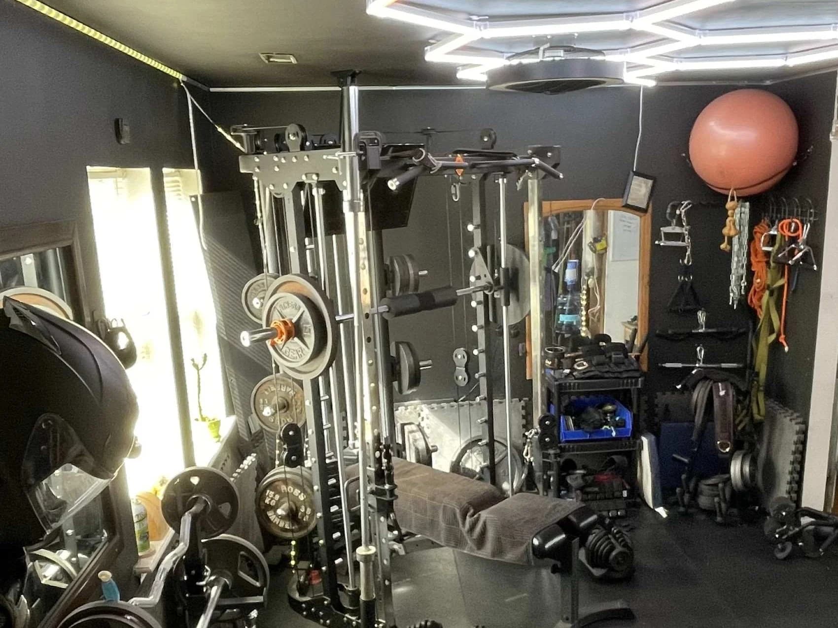 Wall-mounted resistance bands, chains, and a hanging medicine ball beside a power rack and weight bench on a rubber gym floor.