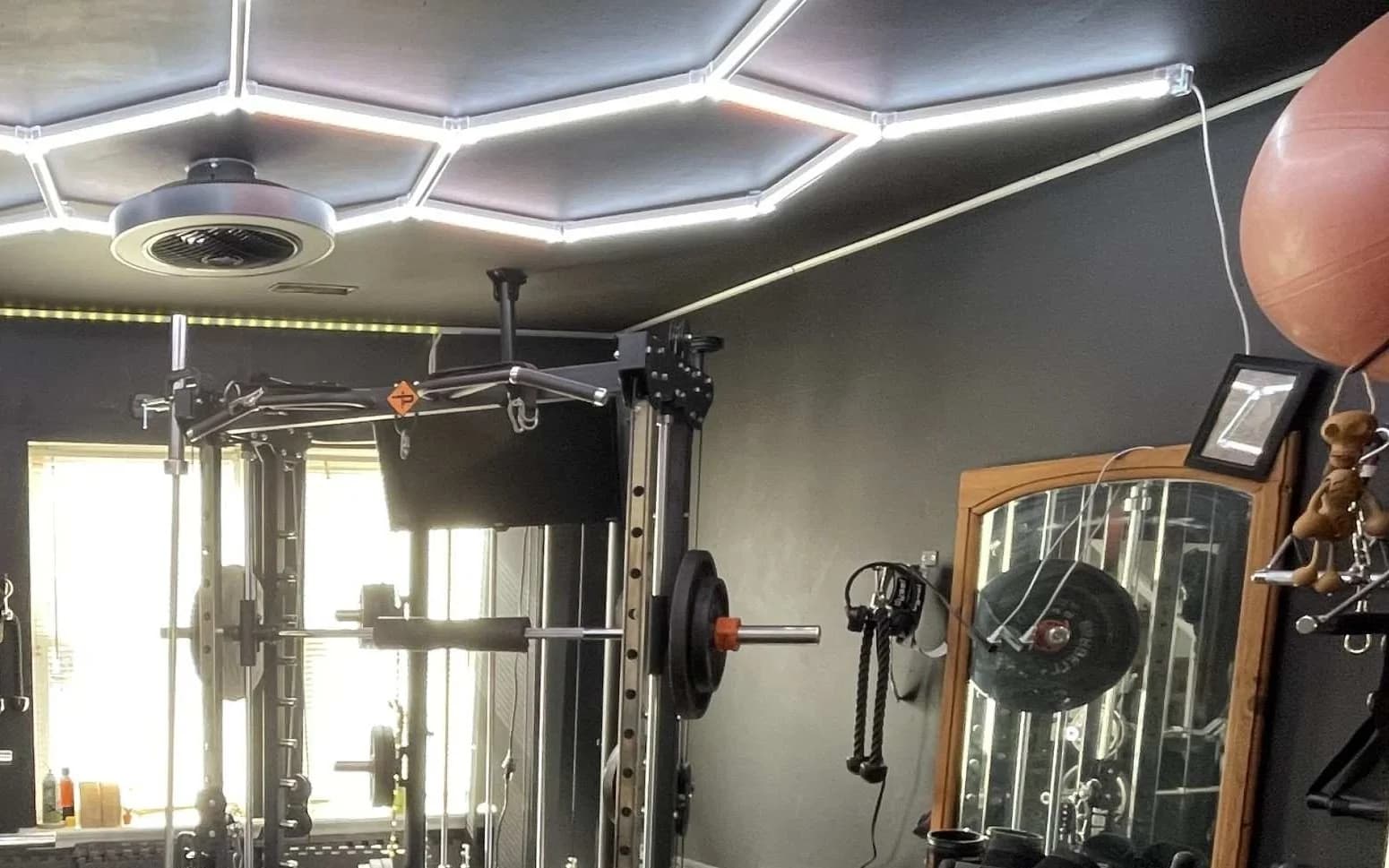 A private gym with a power rack, cable pulley attachment, barbell, and adjustable bench under a hexagonal LED ceiling light.